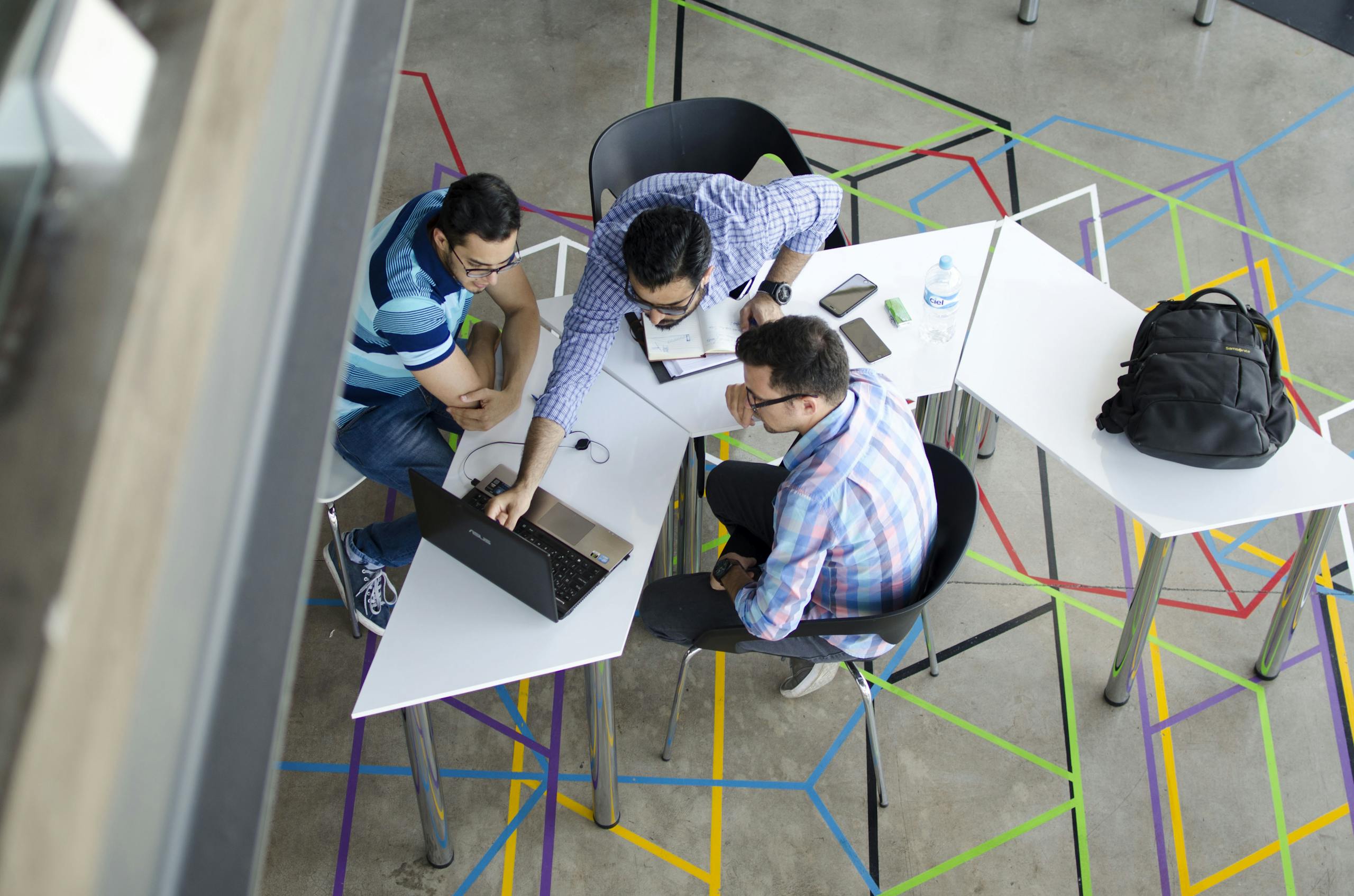 Three men collaborating over a laptop in a modern, geometric-themed office space.